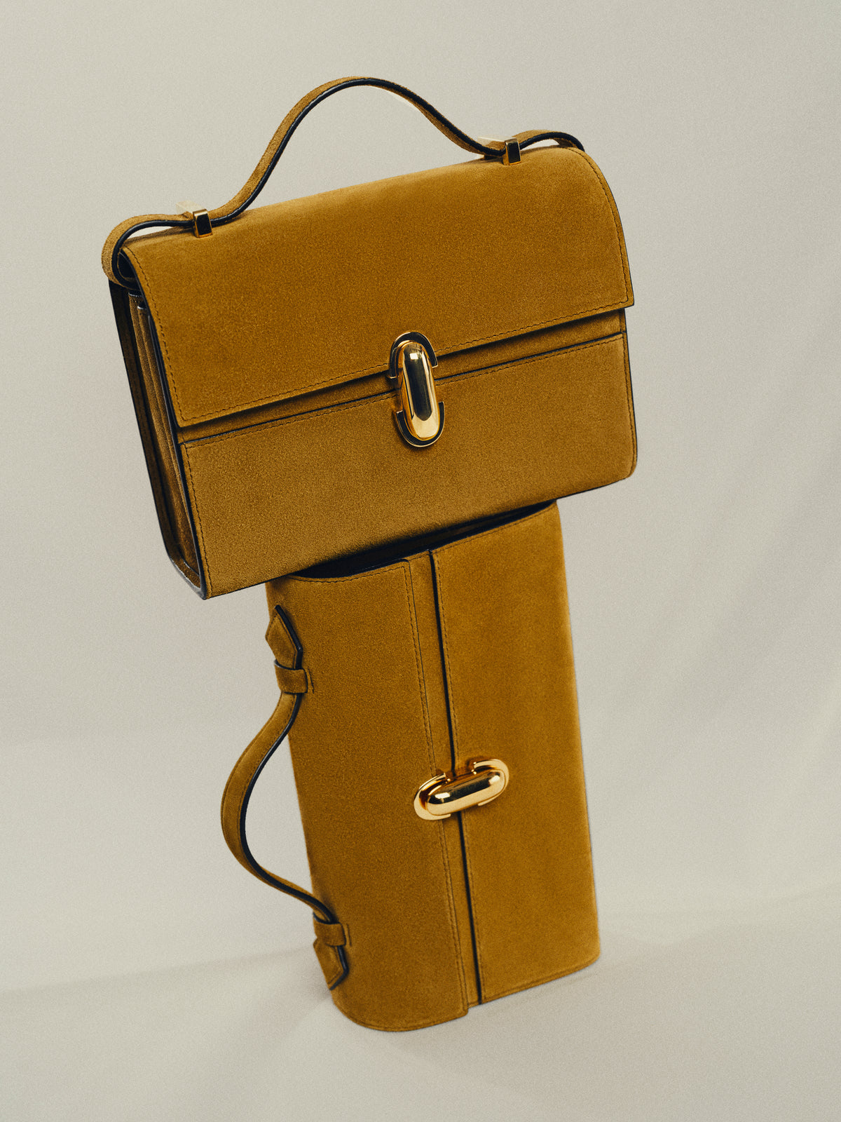campaign image of two sepia brown suede bags with gold hardware on a beige background