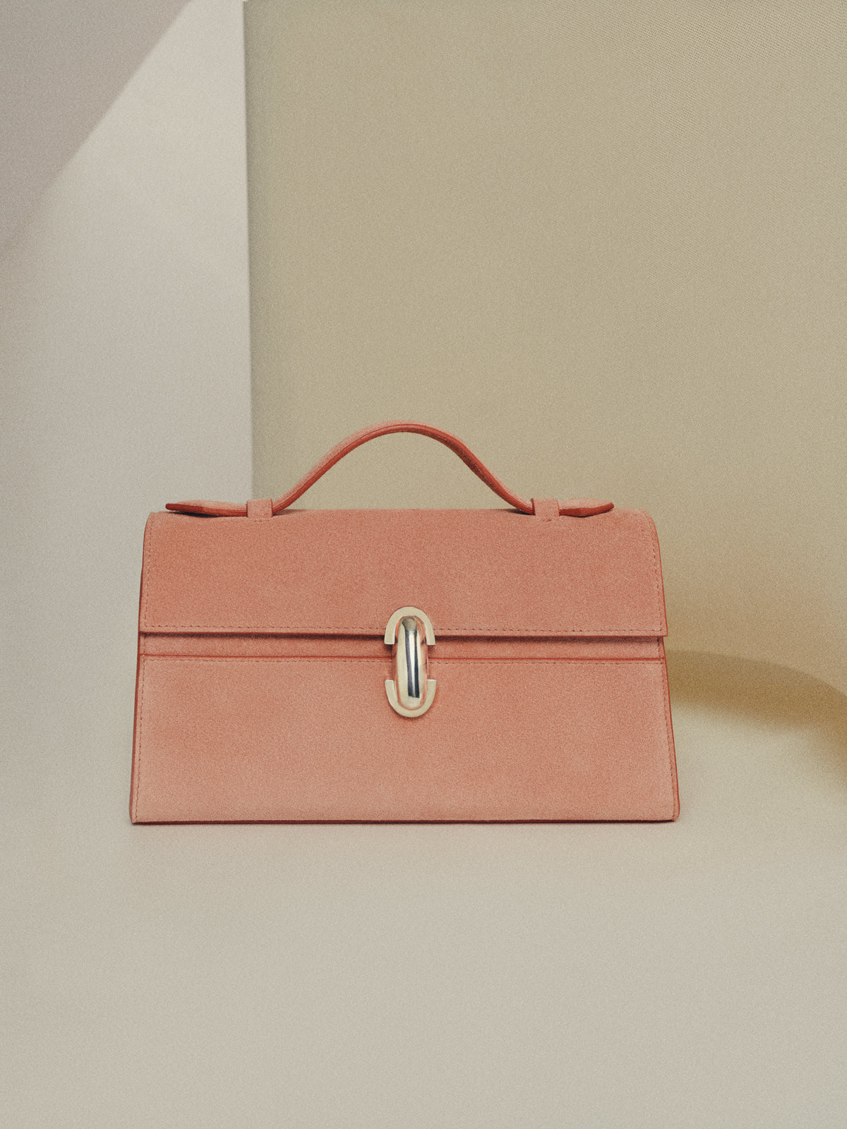 front view of a camelia pink suede bag with silver clasp on a beige background