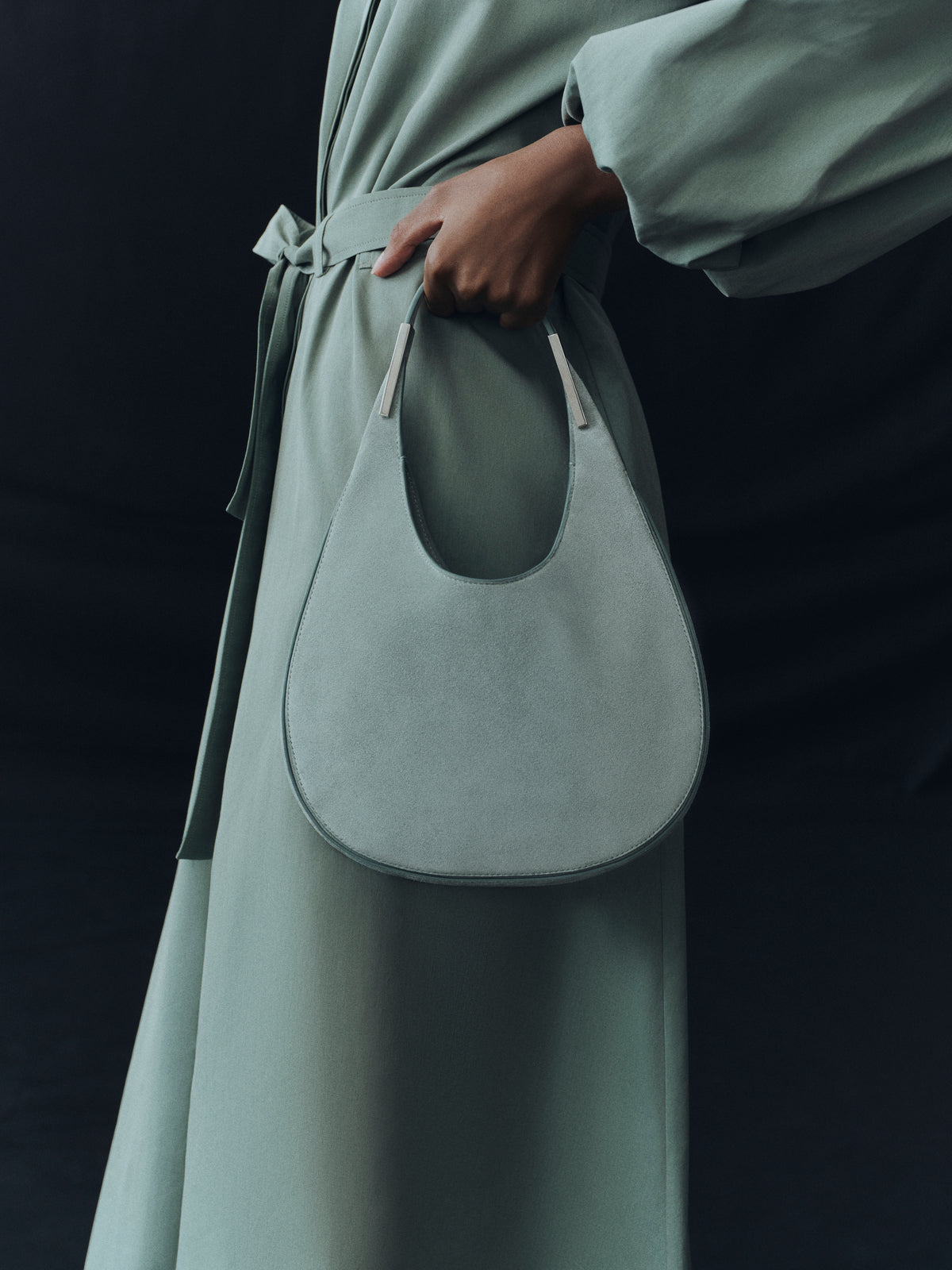 campaign on model image of mist green suede bag with silver hardware on a black background