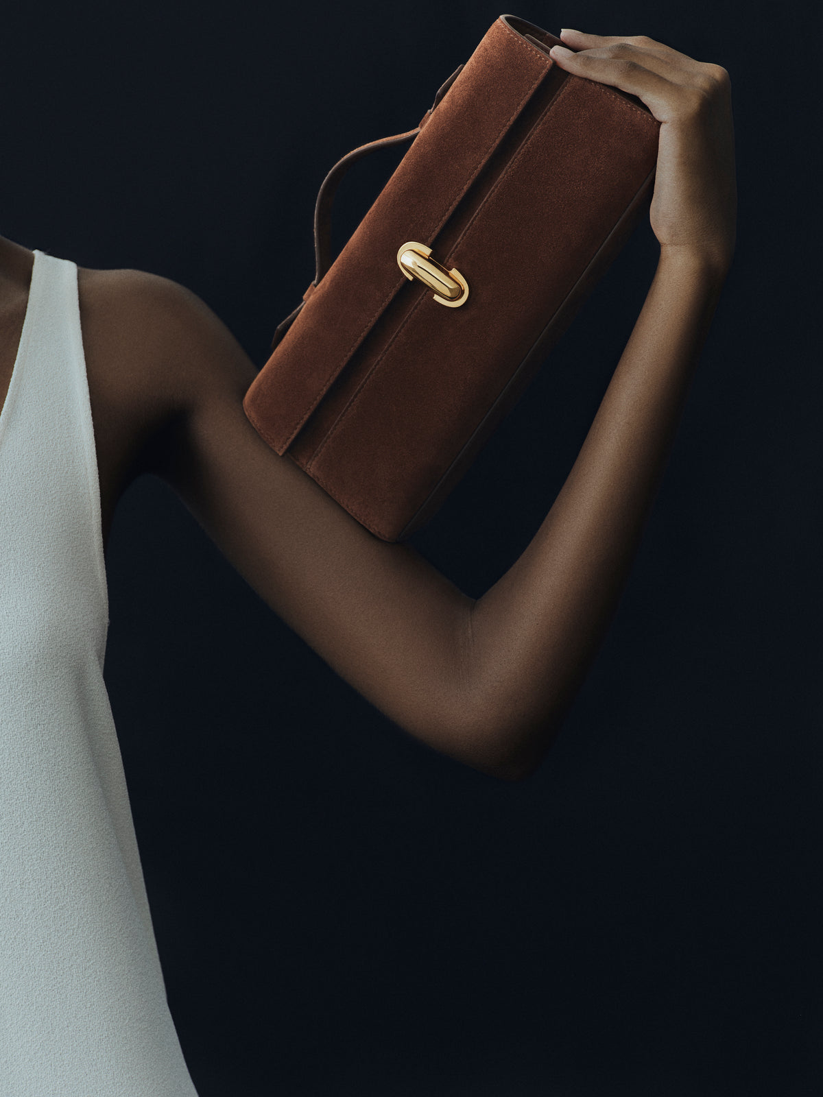 campaign on model image of espresso brown suede bag with gold clasp on a black background