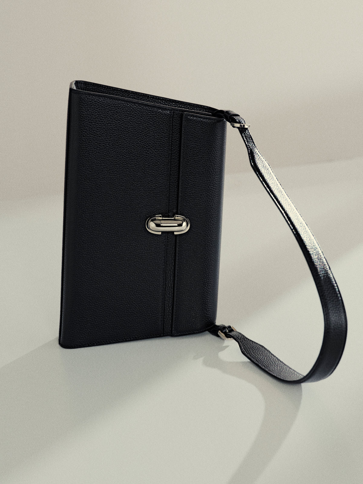campaign image of black grained shoulder bag with silver clasp on an off white background