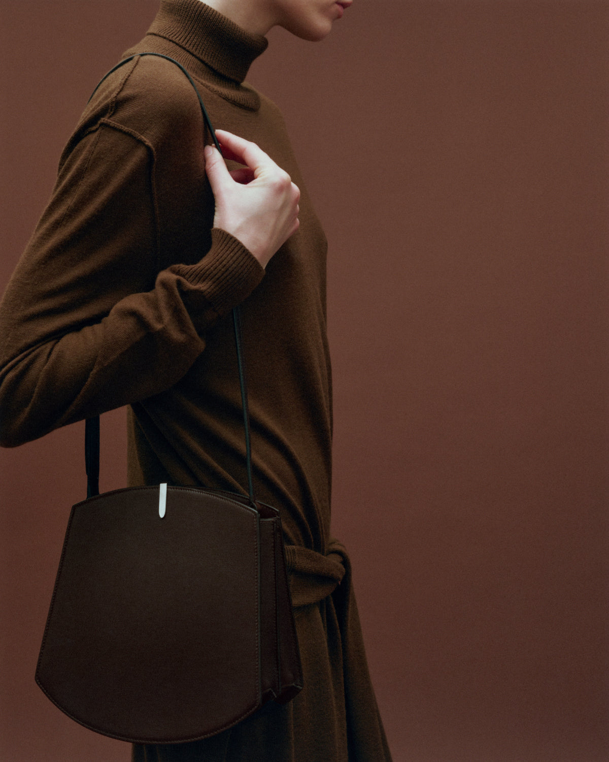 on model image of a brown leather bag with a silver clasp on a brown background