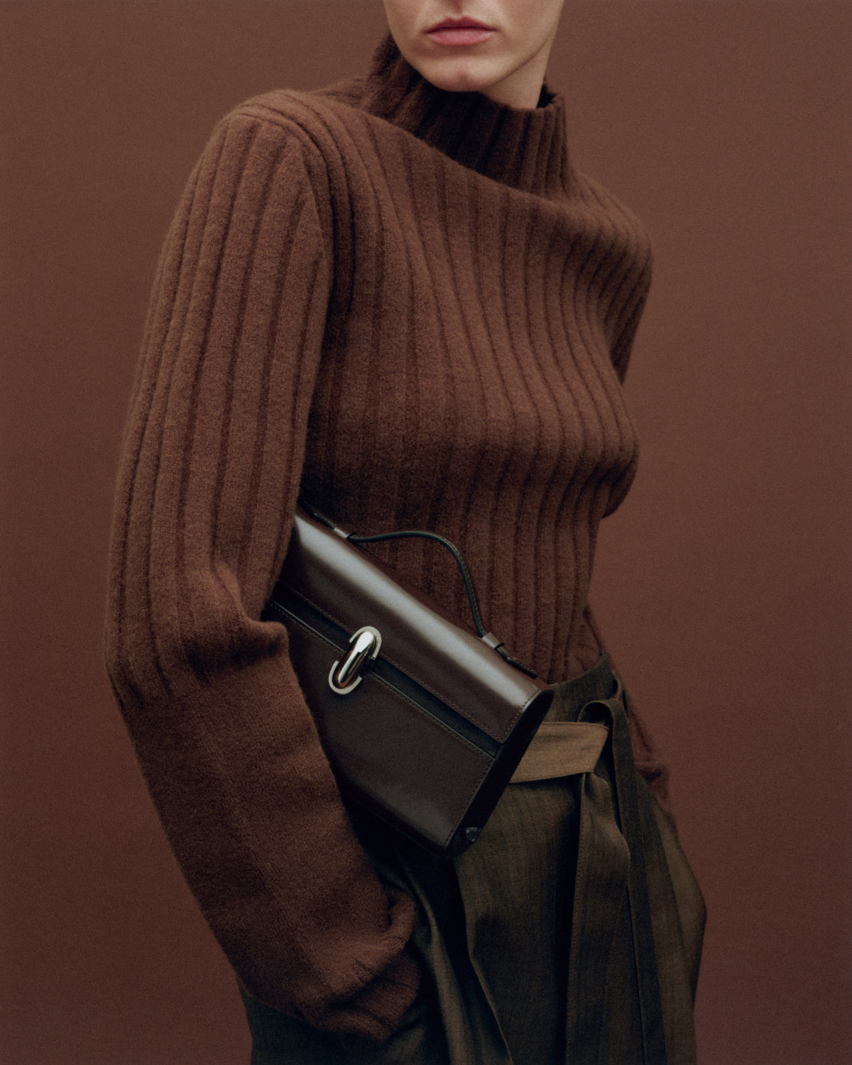 on model image of a brown leather bag with a silver clasp on a brown background