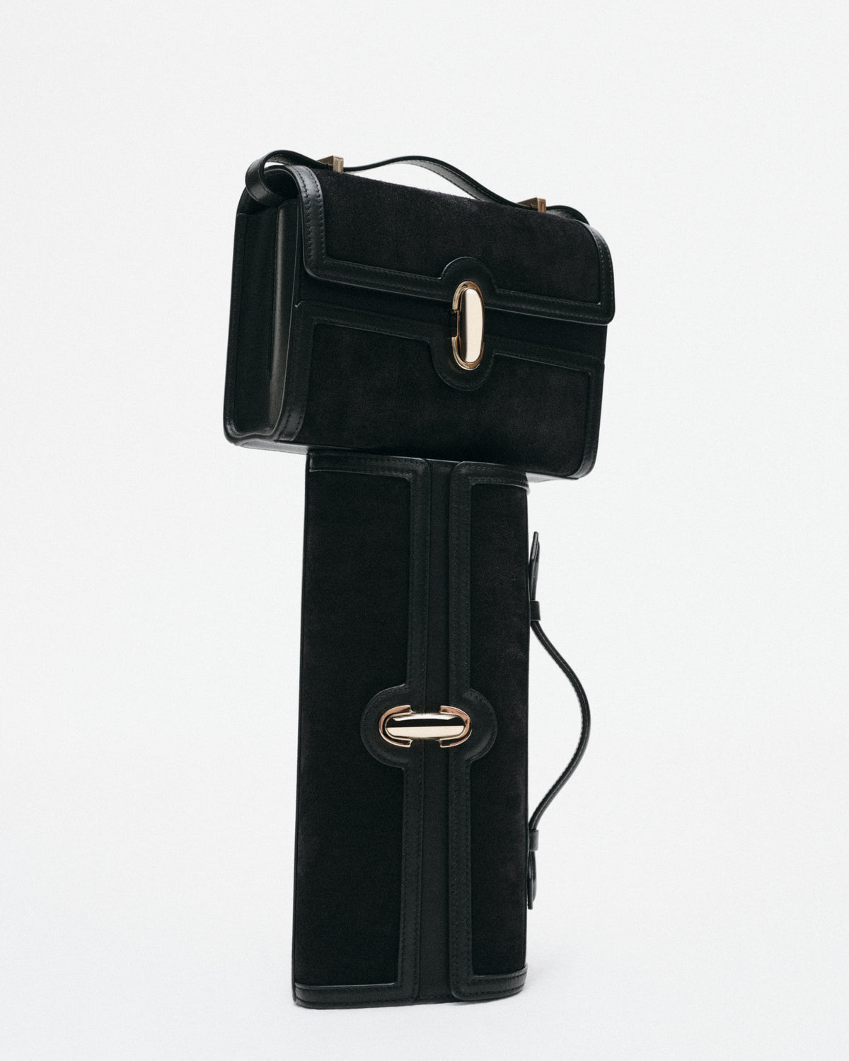 two black suede and leather bags with gold hardware stacked on a white background