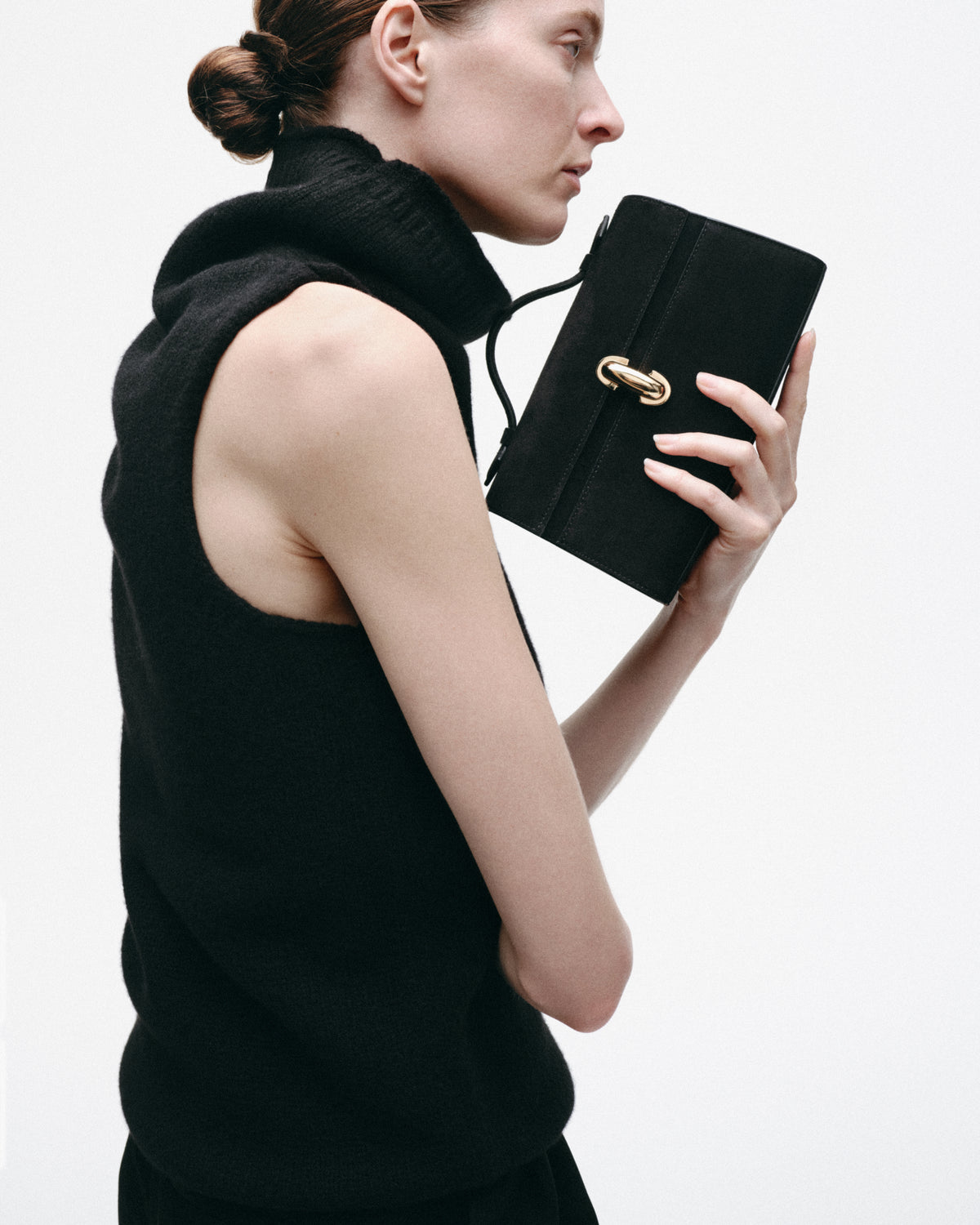 on model image of a black suede handbag with a gold clasp on a white background