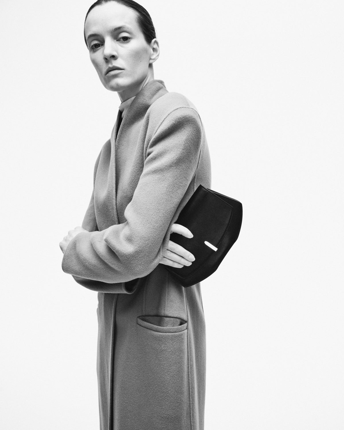 black and white editorial image of model holding a leather clutch on a white background