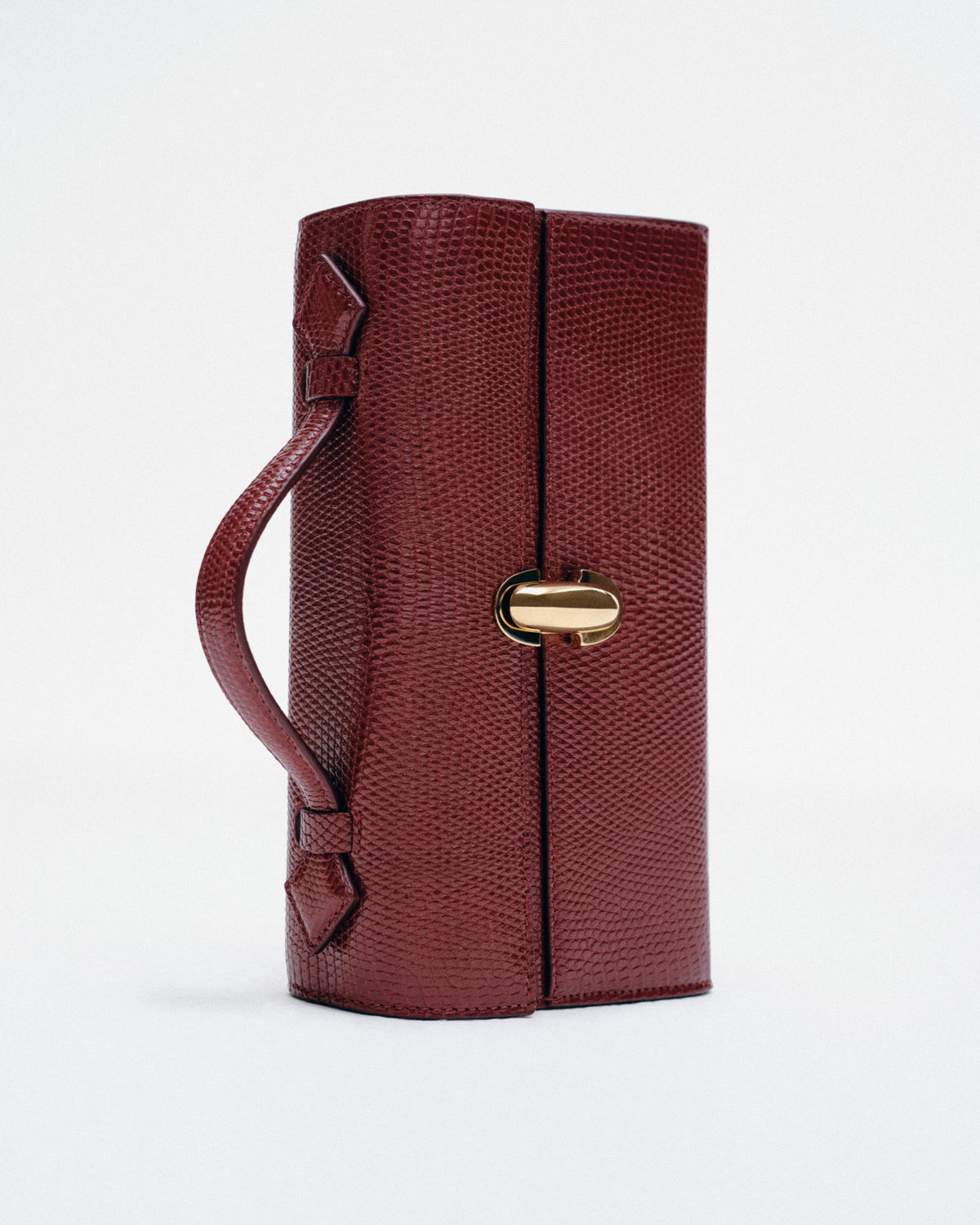 editorial image of a wine red lizard bag with gold clasp on a white background