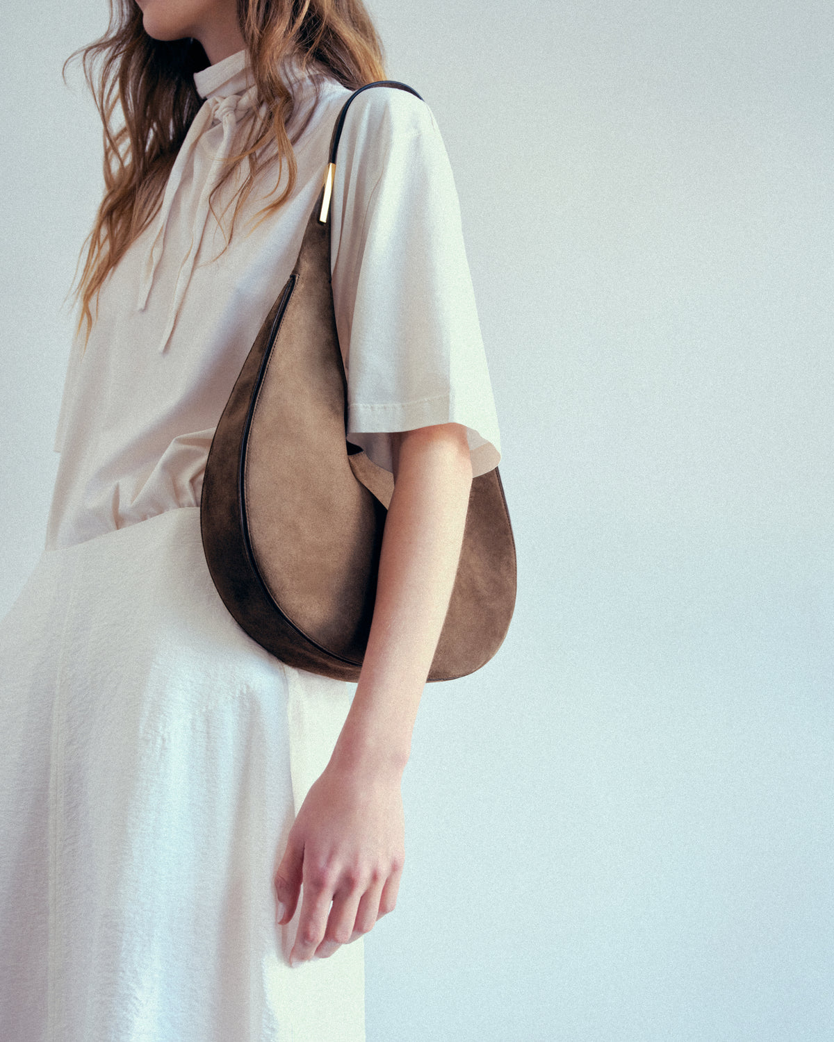 on model image of brown suede bag with gold hardware on a grey background