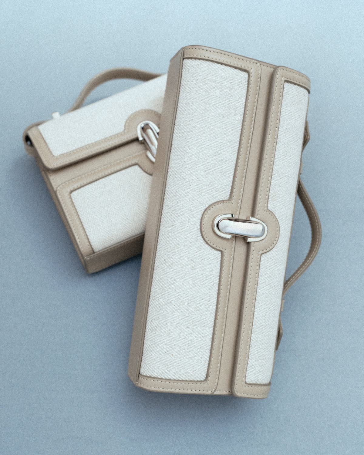 campaign image of two beige canvas bags with leather trim and silver clasp on a grey background