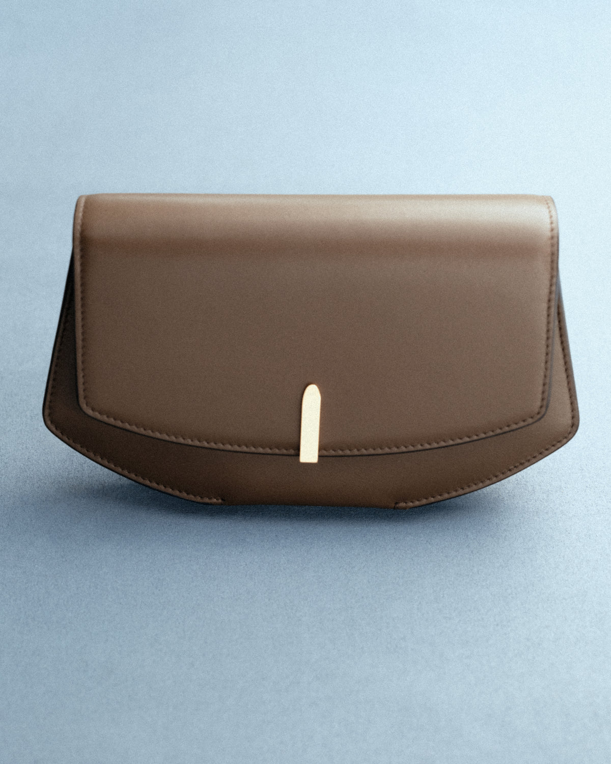 front view of brown clutch with gold hardware on a blue background