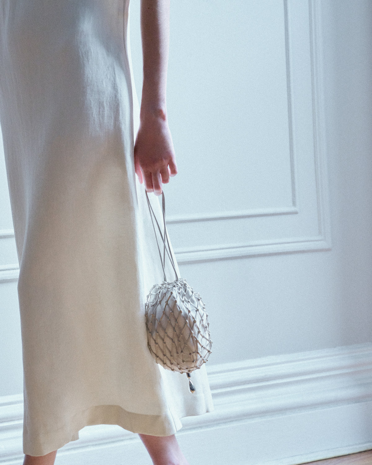 campaign on model image of a bone beige canvas and sheep nappa macrame pouch with silver hardware against a white wall