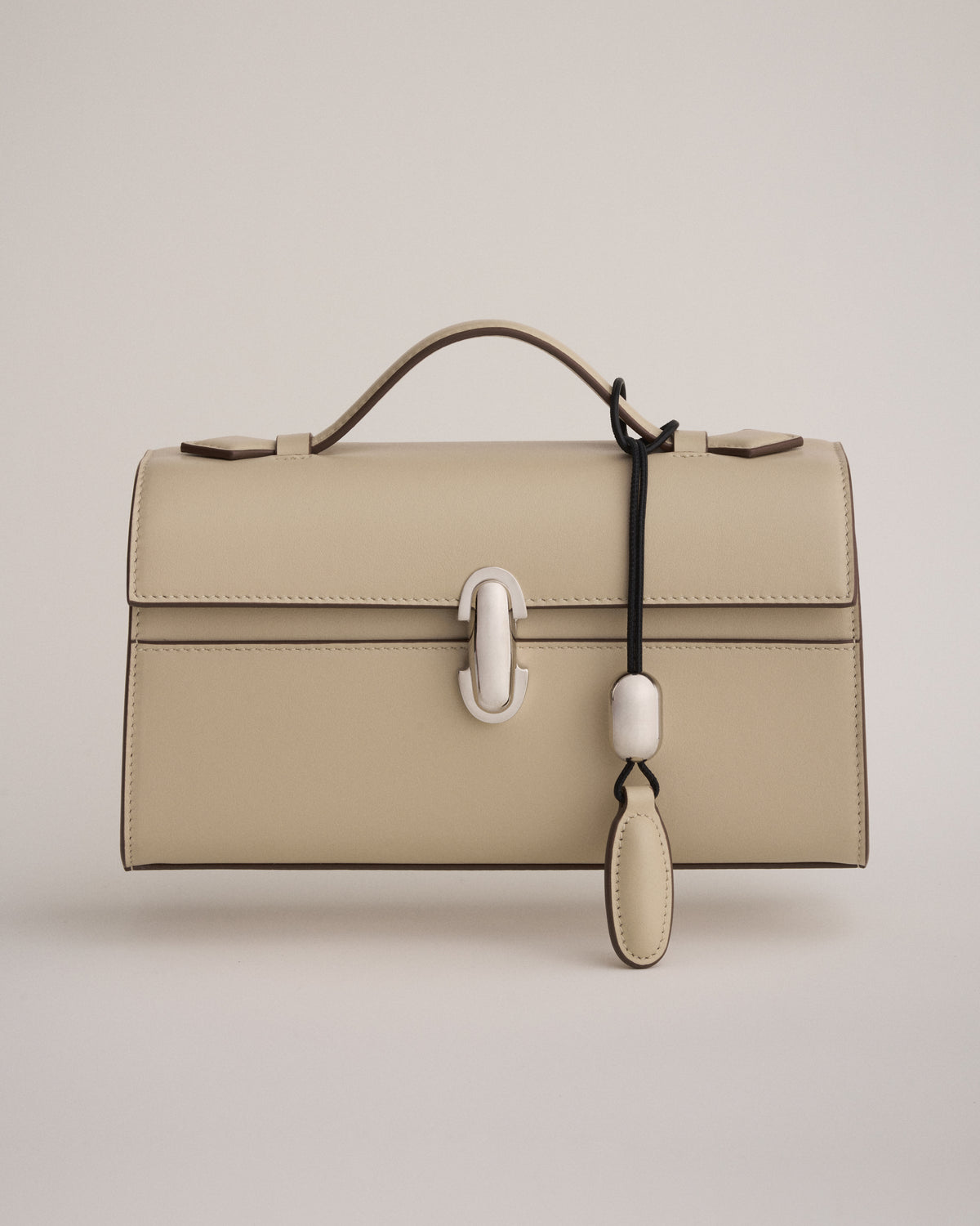 front view of a bone beige leather bag with a silver clasp with a bone beige leather charm on a white background