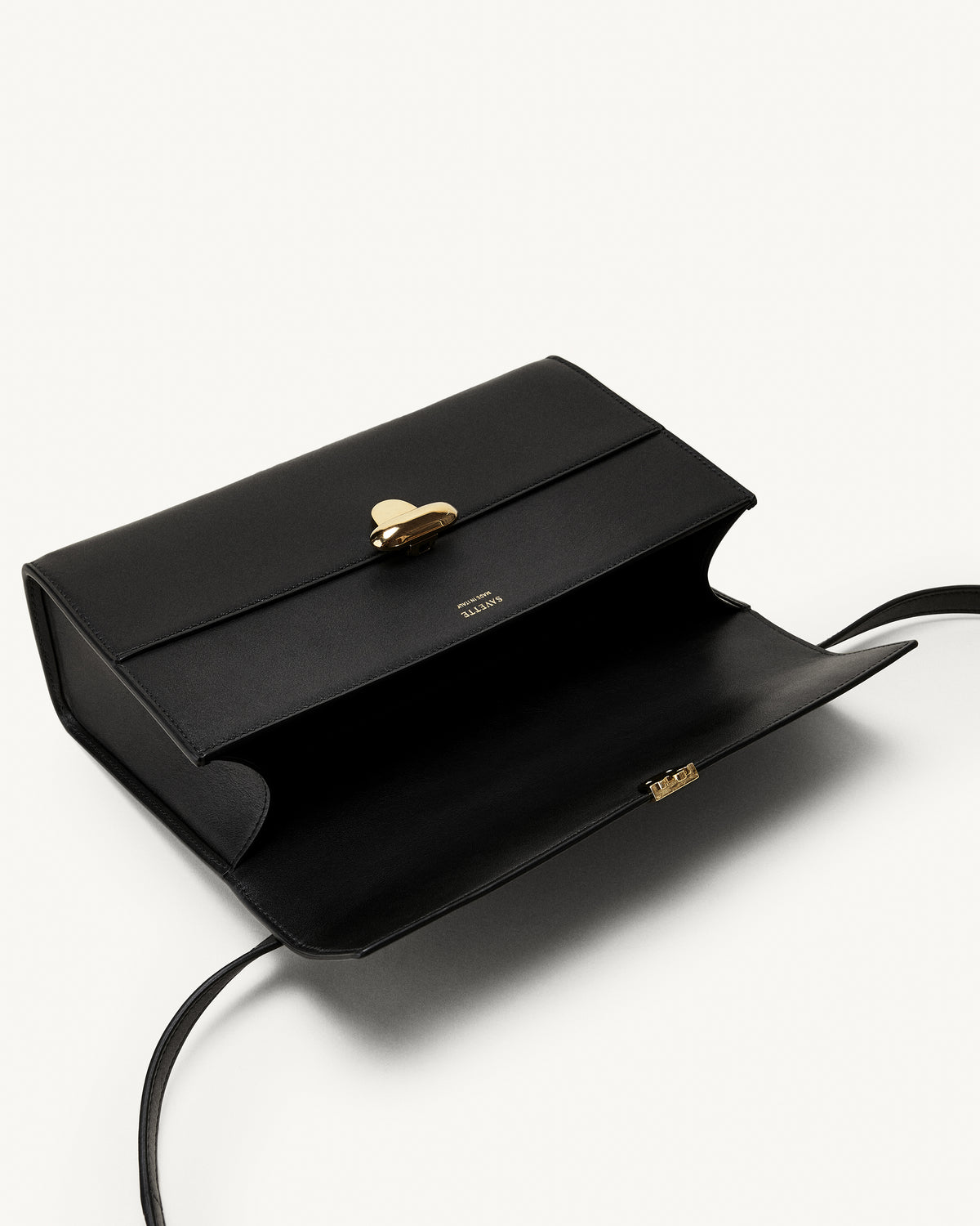 interior view of a black leather bag with a gold clasp on a white background