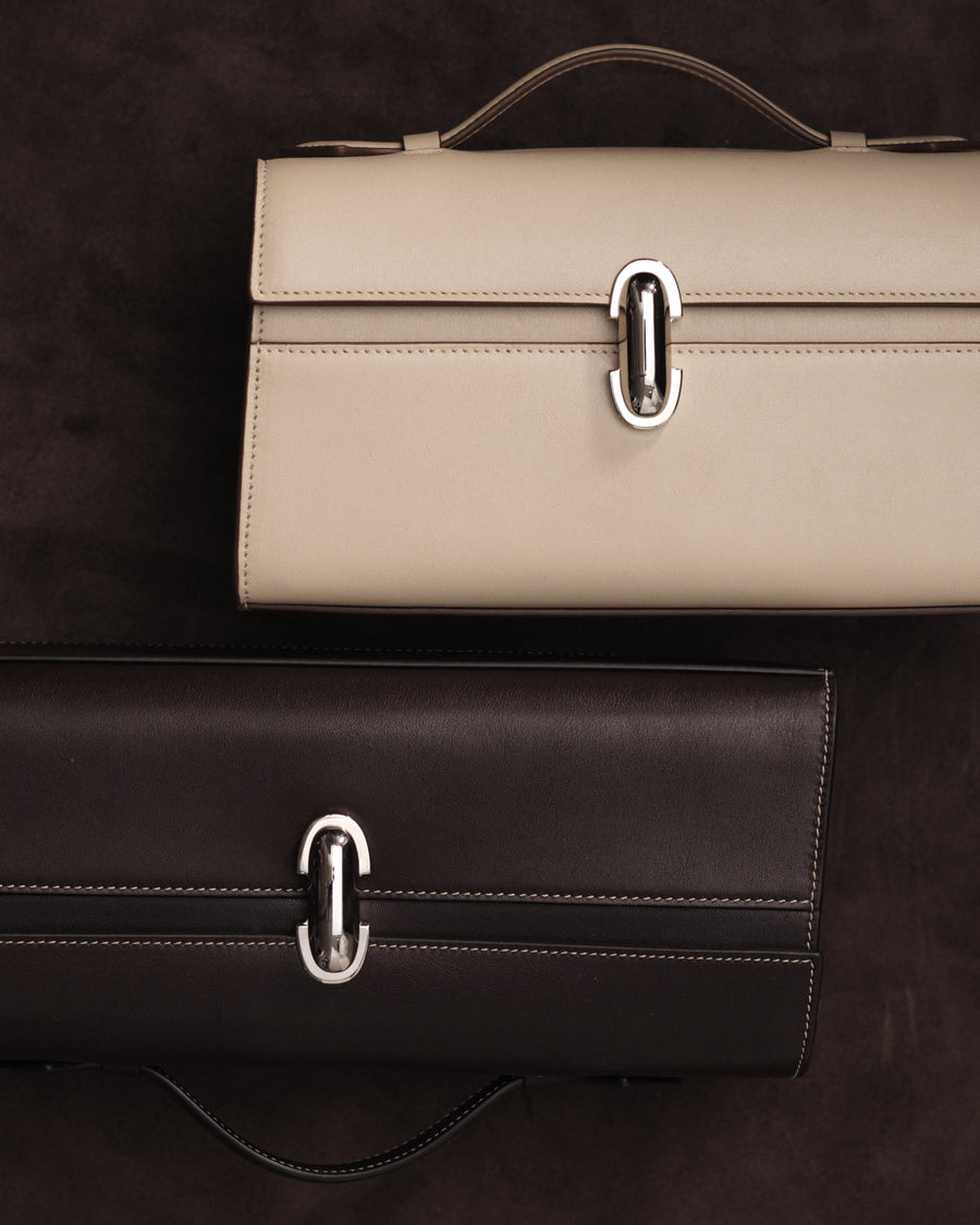 editorial image of a bone beige handbag and currant brown handbag both with silver clasps on a black background