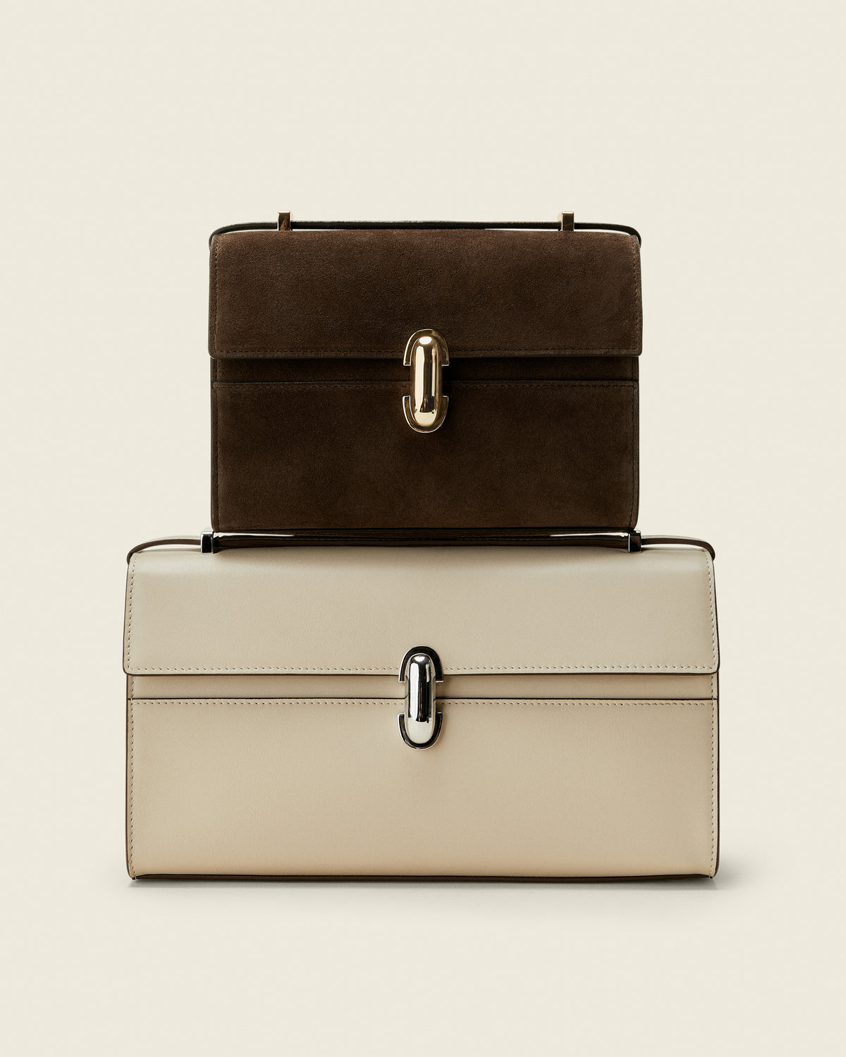 Editorial image of brown suede bag with gold clasp on top of a bone ivory bag with silver clasp on a white background
